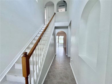 Corridor featuring arched walkways, stairway, a towering ceiling, and light tile patterned floors