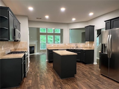 Kitchen with appliances with stainless steel finishes, a sink, light countertops, a center island, and dark wood-style flooring
