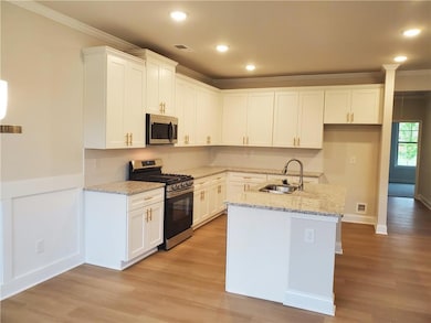 Kitchen featuring appliances with stainless steel finishes, ornamental molding, light stone countertops, white cabinetry, and light wood-style floors
