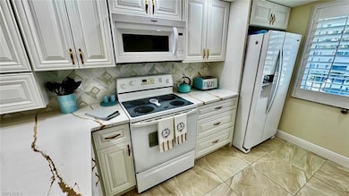Kitchen with white appliances, baseboards, decorative backsplash, and light stone counters