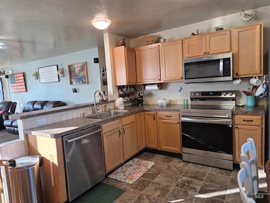 Kitchen with open floor plan, appliances with stainless steel finishes, a peninsula, dark countertops, and a textured ceiling