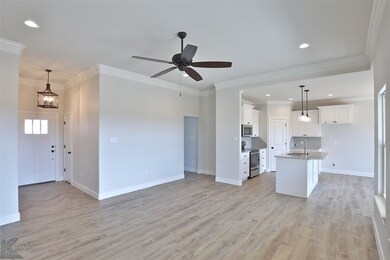 Kitchen featuring appliances with stainless steel finishes, open floor plan, white cabinetry, hanging light fixtures, and crown molding