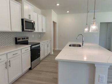Kitchen with appliances with stainless steel finishes, a sink, decorative backsplash, a center island with sink, and light wood-style flooring