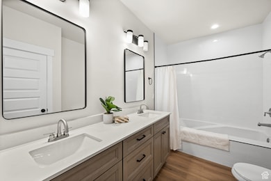 Full bathroom with tiled shower / bath, dark wood-style flooring, double vanity, and recessed lighting