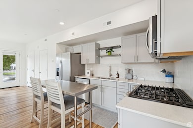 Kitchen featuring tasteful backsplash, light stone countertops, light wood-style flooring, stainless steel appliances, and open shelves