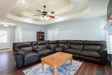 Living room with a raised ceiling, dark wood-style flooring, and ceiling fan