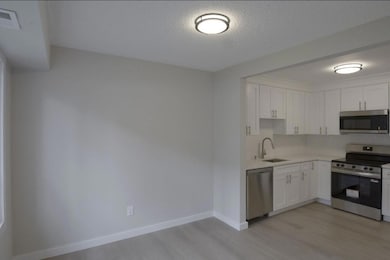 Kitchen featuring stainless steel appliances, light wood finished floors, white cabinetry, and a textured ceiling