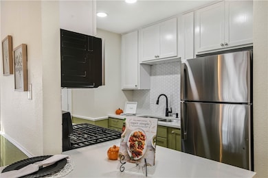 Kitchen featuring freestanding refrigerator, white cabinets, a textured wall, tasteful backsplash, and green cabinetry
