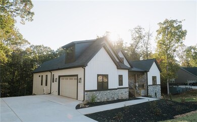 View of front of home with concrete driveway, roof with shingles, stone siding, an attached garage, and board and batten siding