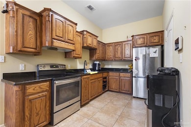Kitchen with stainless steel appliances, brown cabinetry, light tile patterned flooring, and dark stone countertops