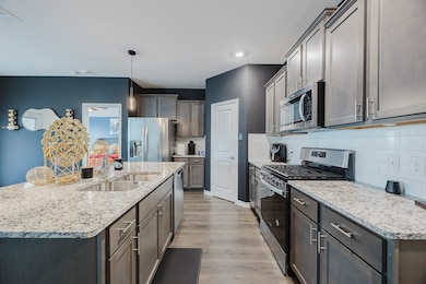Kitchen featuring appliances with stainless steel finishes, pendant lighting, light wood-style flooring, a kitchen island with sink, and light stone counters