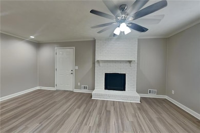 Unfurnished living room featuring wood finished floors, a ceiling fan, recessed lighting, a brick fireplace, and ornamental molding
