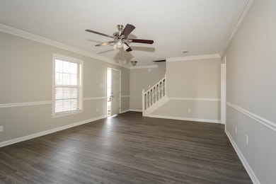Unfurnished living room with crown molding, dark wood finished floors, stairs, and a ceiling fan