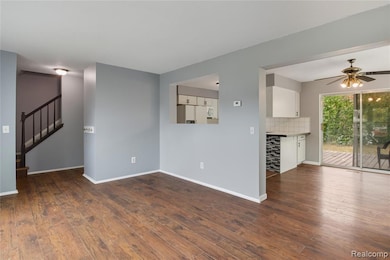Unfurnished living room with stairway, a ceiling fan, and dark wood-type flooring