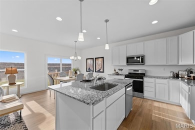 Kitchen featuring light stone countertops, white cabinetry, appliances with stainless steel finishes, a kitchen island with sink, and light wood-style flooring