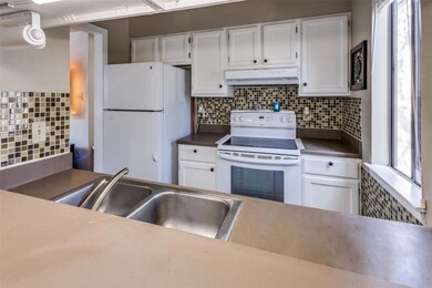 Kitchen with under cabinet range hood, a sink, white appliances, white cabinets, and decorative backsplash