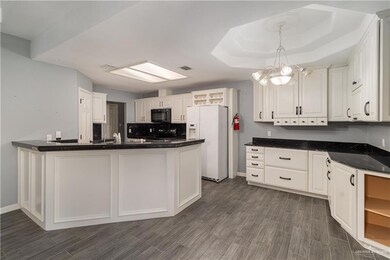 Kitchen with black appliances, a peninsula, white cabinets, and dark wood finished floors