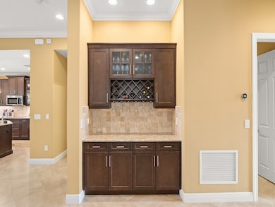 Indoor dry bar featuring dark brown cabinets, backsplash, glass insert cabinets, light stone countertops, and recessed lighting