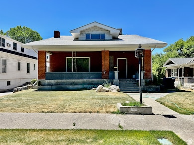 Bungalow-style home featuring a porch, brick siding, a chimney, and a front yard
