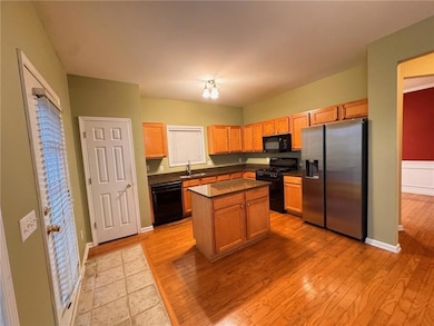 Kitchen featuring black appliances, light wood-type flooring, a center island, and brown cabinets