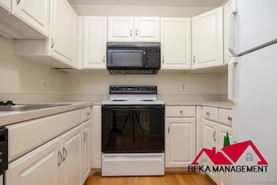 Kitchen with freestanding refrigerator, electric stove, white cabinetry, black microwave, and light countertops