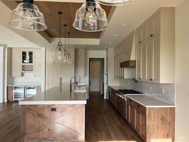 Kitchen with hanging light fixtures, a large island with sink, backsplash, light stone countertops, and dark wood finished floors