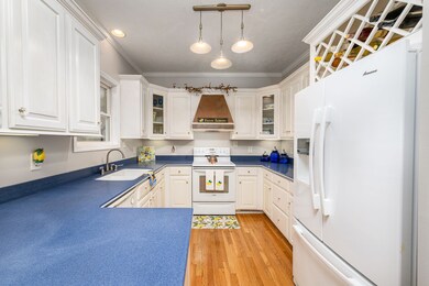 The kitchen features custom white cabinets with wine rack & glass door accents, copper hood, deep farmhouse sink, solid surface countertops, under cabinet lighting, breakfast bar and french door refrigerator less than 2 years old.