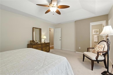 Bedroom featuring a tray ceiling, light colored carpet, and a ceiling fan