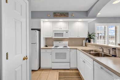 Kitchen featuring light tile patterned floors, a textured ceiling, white appliances, a sink, and white cabinets