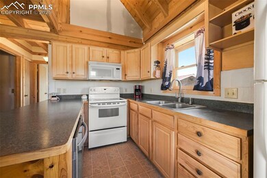 Kitchen featuring white appliances, dark countertops, light brown cabinetry, wood ceiling, and a peninsula