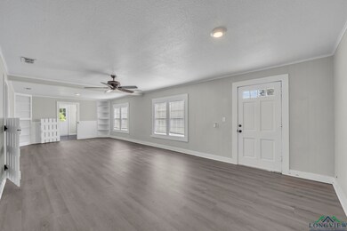 Unfurnished living room with a textured ceiling, baseboards, healthy amount of natural light, wood finished floors, and ornamental molding
