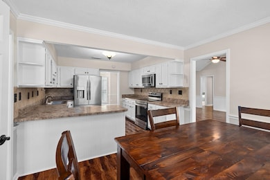 Kitchen featuring appliances with stainless steel finishes, open shelves, a peninsula, white cabinetry, and ornamental molding