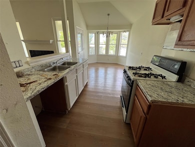 Kitchen featuring range with gas stovetop, dark wood finished floors, vaulted ceiling, a chandelier, and hanging light fixtures