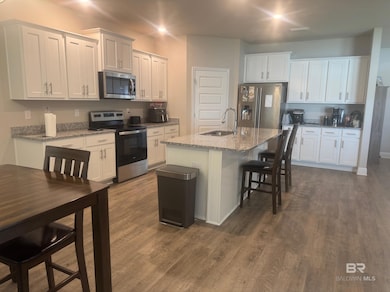 Kitchen with appliances with stainless steel finishes, white cabinetry, and an island with sink