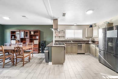 Kitchen with stainless steel appliances, dark stone counters, a peninsula, island exhaust hood, and a textured ceiling