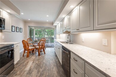 Kitchen with stainless steel appliances, dark wood-style flooring, ornamental molding, white cabinetry, and light stone counters