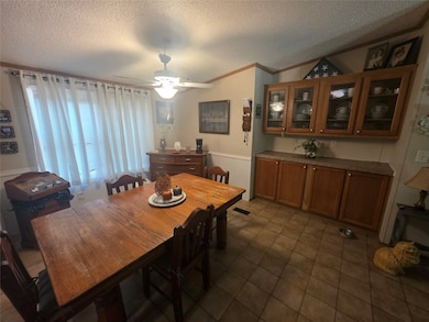 Dining area with a textured ceiling, ceiling fan, wainscoting, and crown molding