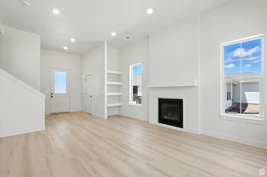 Unfurnished living room featuring recessed lighting, a glass covered fireplace, light wood-type flooring, and built in features