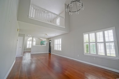 Unfurnished living room with a high ceiling, a chandelier, plenty of natural light, wood finished floors, and baseboards