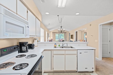 Kitchen with white cabinets, white appliances, a peninsula, a chandelier, and vaulted ceiling