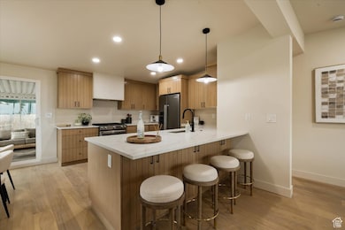 Kitchen with a breakfast bar area, light wood-type flooring, a peninsula, stainless steel appliances, and baseboards