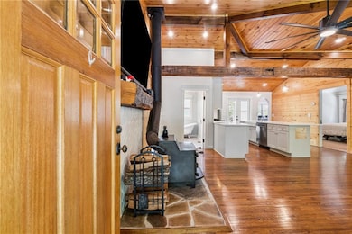 Living room with wood ceiling, a wood stove, wood walls, ceiling fan, and dark wood-style floors