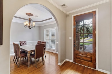 Dining room with ornamental molding, a chandelier, wood finished floors, arched walkways, and a tray ceiling