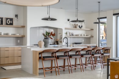 Kitchen with open shelves, an island with sink, light countertops, a kitchen breakfast bar, and modern cabinets