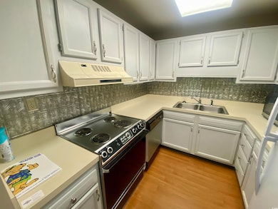 Kitchen with black electric range oven, range hood, light countertops, white cabinetry, and light wood-style floors