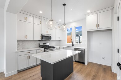 Kitchen featuring white cabinets, a center island, stainless steel appliances, decorative light fixtures, and tasteful backsplash