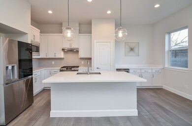 Contemporary kitchen with quartz countertops, stainless steel appliances, ample cabinetry, and breakfast bar seating—stylishly finished with continuous wood-look tile flooring.