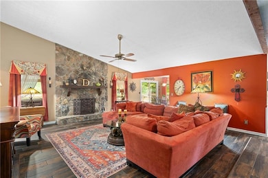 Living area with vaulted ceiling, a stone fireplace, hardwood / wood-style flooring, and ceiling fan