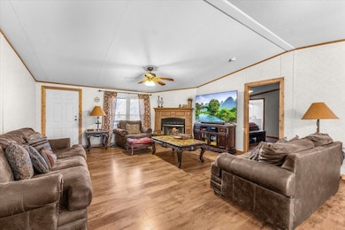 Living room with crown molding, light wood finished floors, a warm lit fireplace, vaulted ceiling, and ceiling fan