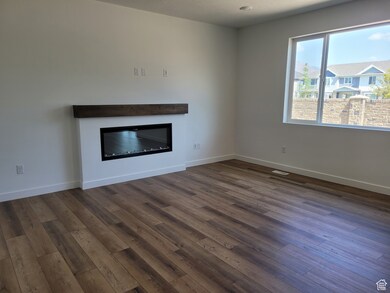 Unfurnished living room with a glass covered fireplace and dark wood-style flooring